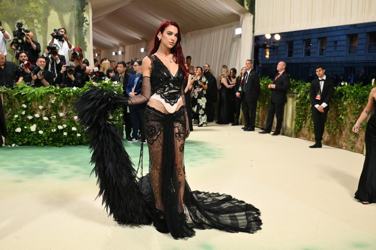 Dua Lipa made a grand entrance on the MET Gala carpet, wrapped in black feathers, statement earrings, and intricate lace from Marc Jacobs.