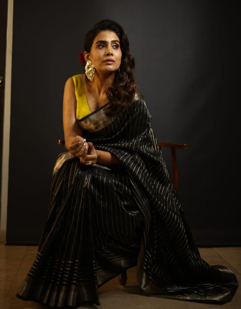 Kulkarni wears a classic black saree with zari work, paired with a yellow sleeveless blouse which adds a pop of colour. She completes her look with chunky gold earrings and a red rose on her hair. Minimal accessories make the look stand out.