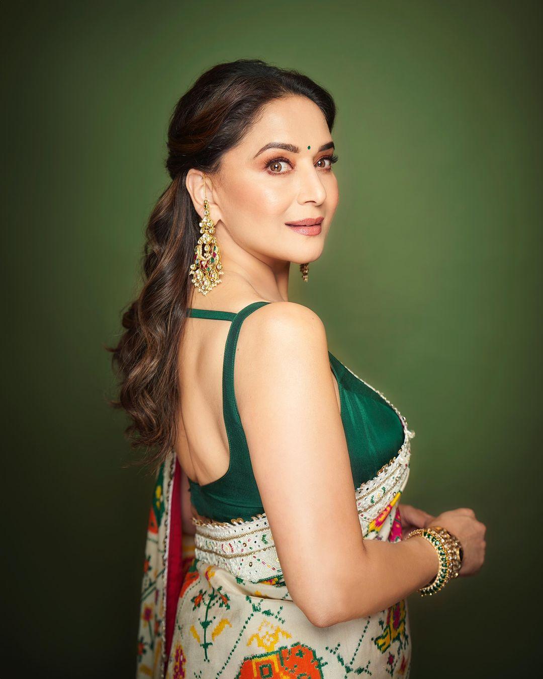 To elevate her appearance, Madhuri paired this saree with a strappy green blouse that establishes a perfect contrast. She left her hair open in a half clutch and carried a matching potli to complete the look