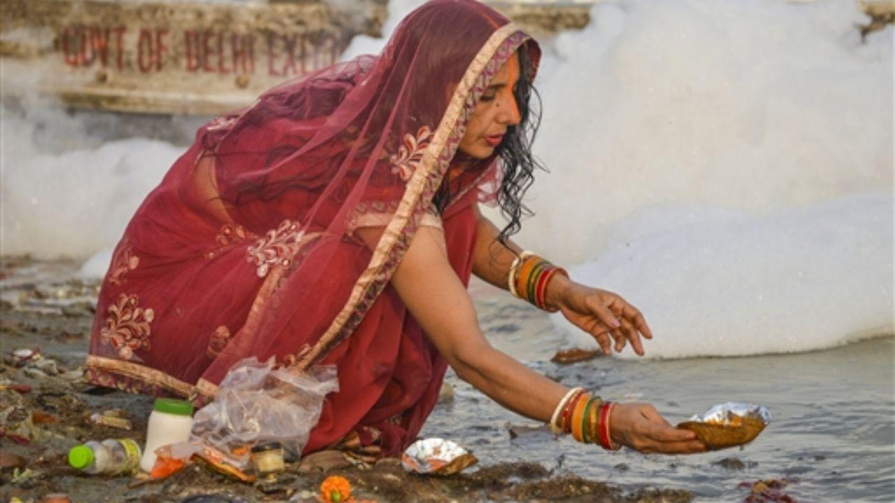 A devotee performs rituals on the bank of the Yamuna river as toxic foam floats on the surface of the polluted river at Kalindi Kunj in New Delhi