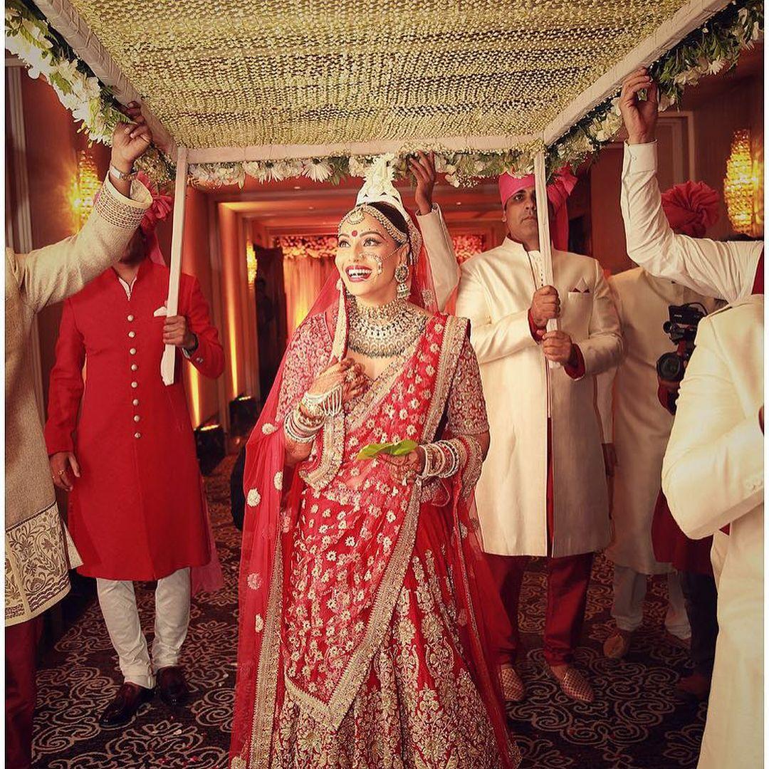 Bipasha Basu opted for a traditional red and gold bridal look by Sabyasachi, featuring a heavily embellished lehenga and blouse with intricate gold zari work. She accessorized with statement kundan jewelry from Jaipur Jewels.