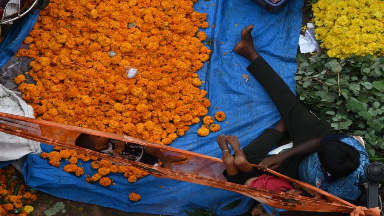 A man rocks a cloth cradle while making sales at the market