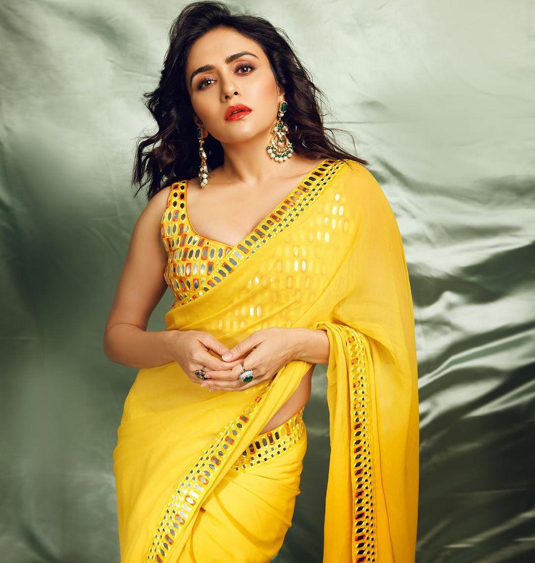 In this look, the actress wore a plain yellow saree with mirrorwork on the borders. She paired the saree with a strappy blouse embedded with mirrors and featuring a contrasting brown colour