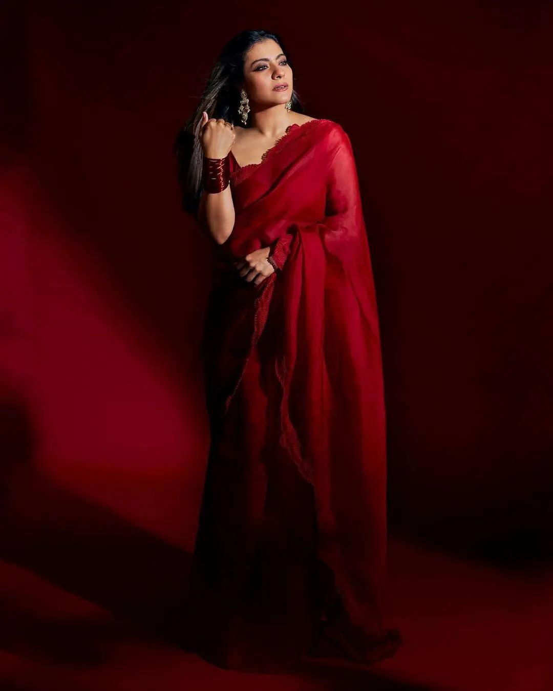 On Ashtami, as the festive excitement hits its peak, this outfit on Kajol makes for the perfect choice. She dons a stunning scarlet red saree, elegantly paired with a sleeveless blouse featuring a delicate scalloped border.