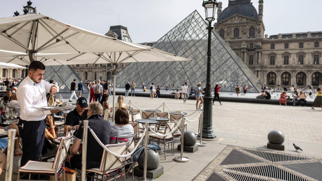 A waiter serves a drink in a restaurant terrace near the Louvre Pyramid, designed by Chinese-US architect Ieoh Ming Pei, at the Louvre Museum