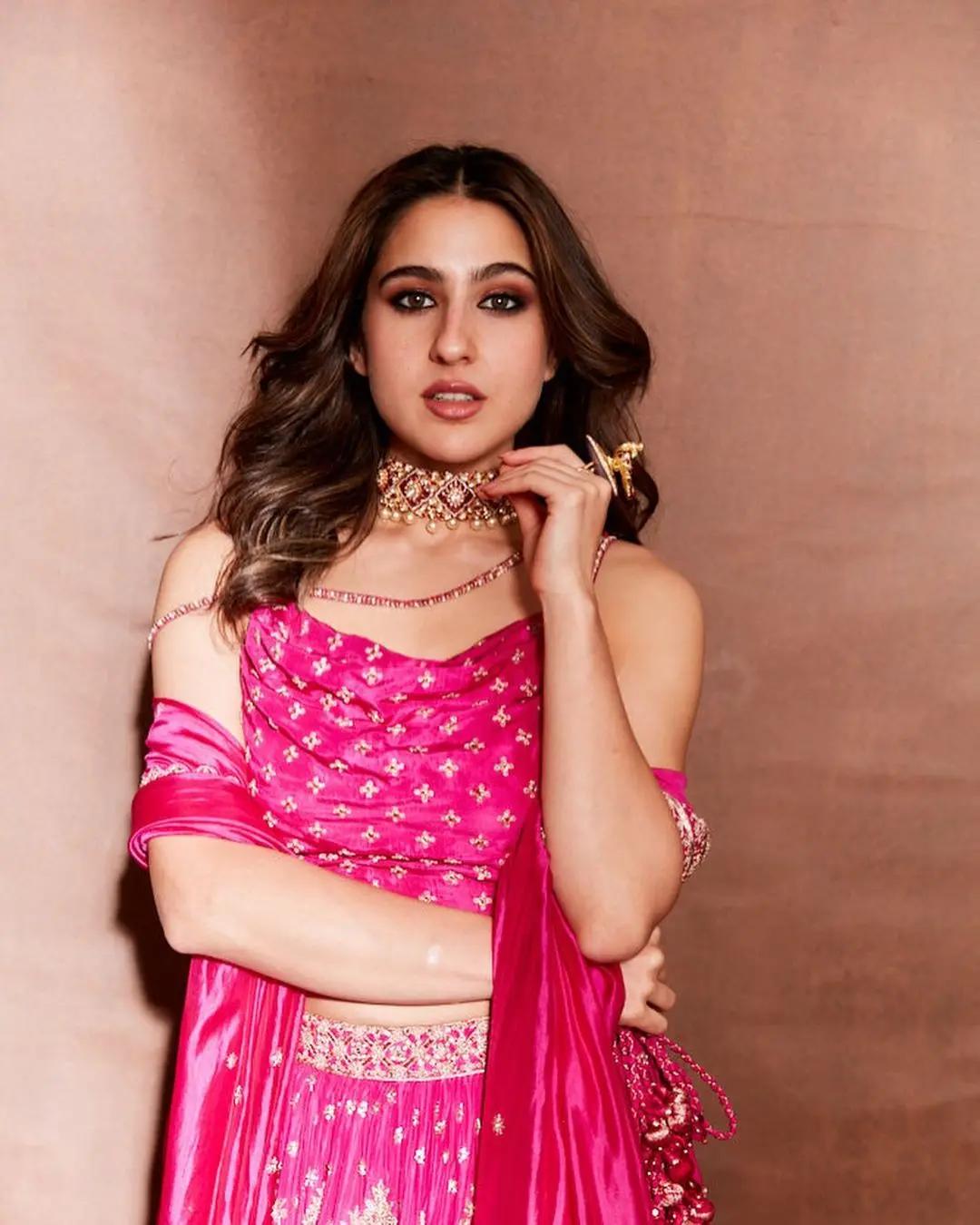 This outfit on Sara makes for the perfect Saptami evening ensemble. It is truly inspiring for anyone aiming to nail the perfect Saptami look. She's donning a lovely ensemble – a pink slip blouse with a chic asymmetrical hem and a long, flowing pink silk skirt that's beautifully adorned with golden details at the waist. 