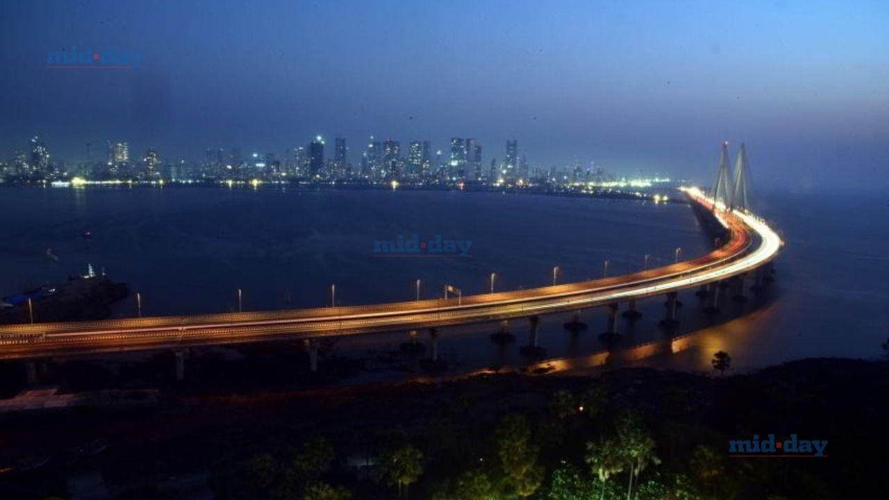 The city’s bustling streets glow with golden trails of headlights, while high-rises shimmer against the deep blue sky, reflecting the energy of a metropolis that never sleeps
