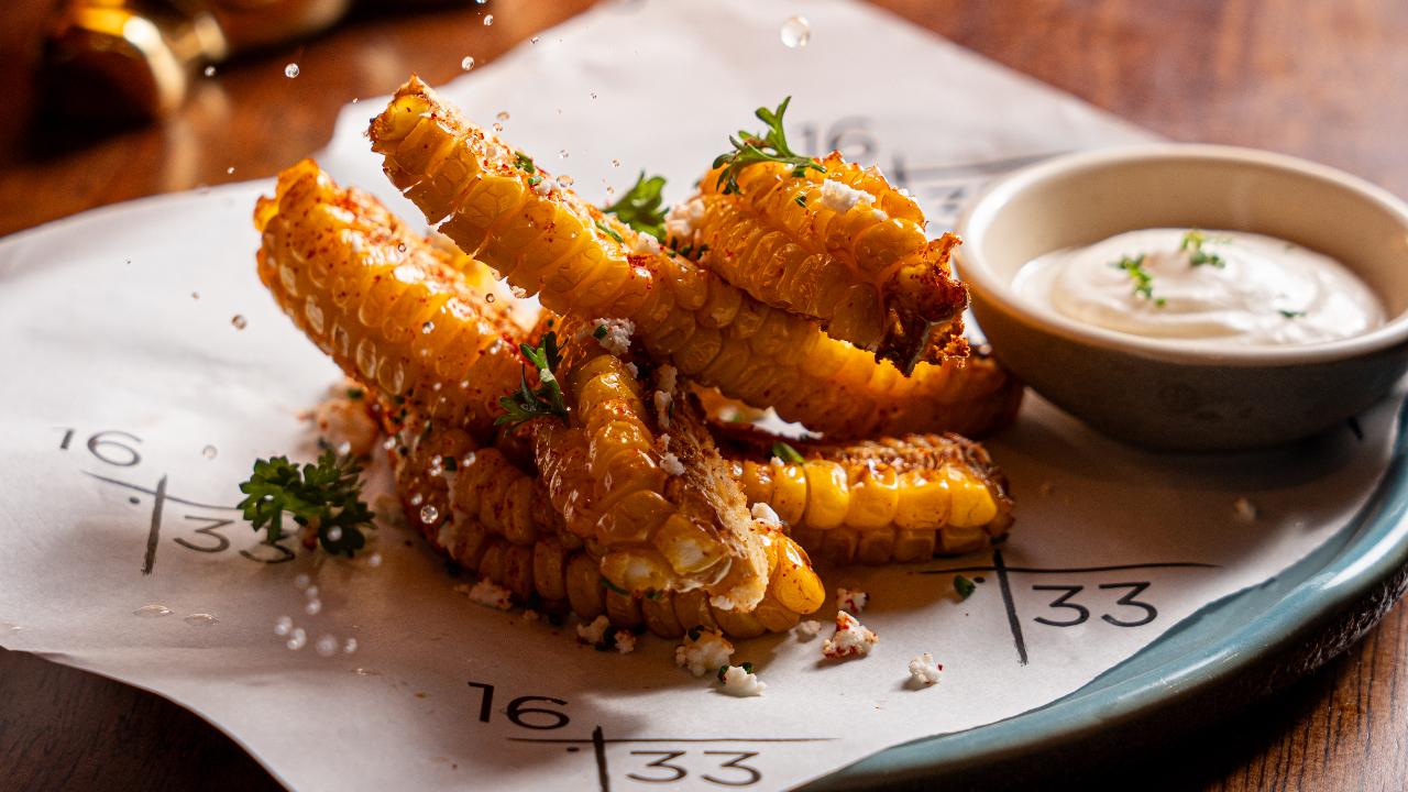 Corn Ribs with Chilli Lemon Butter, Smoked Paprika and Salted FetaChef Anil Gawas at Sixteen33 in Bandra says you can make Corn Ribs with Chilli Lemon Butter, Smoked Paprika and Salted Feta. The corn ribs are quartered corn cobs fried until crispy and slightly curled. They're coated in a smoky, spiced paprika butter—a blend of melted butter, smoked paprika, and citrusy lemon. Served with a side of creamy garlic aioli for dipping.
Use 2 corn on the cob (boiled, husked, ends trimmed), butter (melted) 2 tbsp, Smoked paprika 1 tsp, Salt (adjust to taste), Lemon juice (plus extra wedges for serving) 1 tbsp, and Garlic aioli (for dipping) 2 tbsp
Then Cut each cob into quarters lengthwise (this is what helps them curl when cooked). A sharp chef’s knife or cleaver works best—rock it through carefully. You’ll end up with 6 rib shaped pieces. In a bowl, combine the melted butter, smoked paprika, lemon juice, and salt. Brush this over the ribs. Cook the ribs in a deep fat fryer at 180 degrees Celsius (350 degrees Fahrenheit) for 4-5 minutes until curled and crispy at the edges. Place ribs cut side down. Once done, brush with a little extra butter if desired. Serve hot with garlic aioli on the side for dipping, and extra lemon wedges to squeeze over.