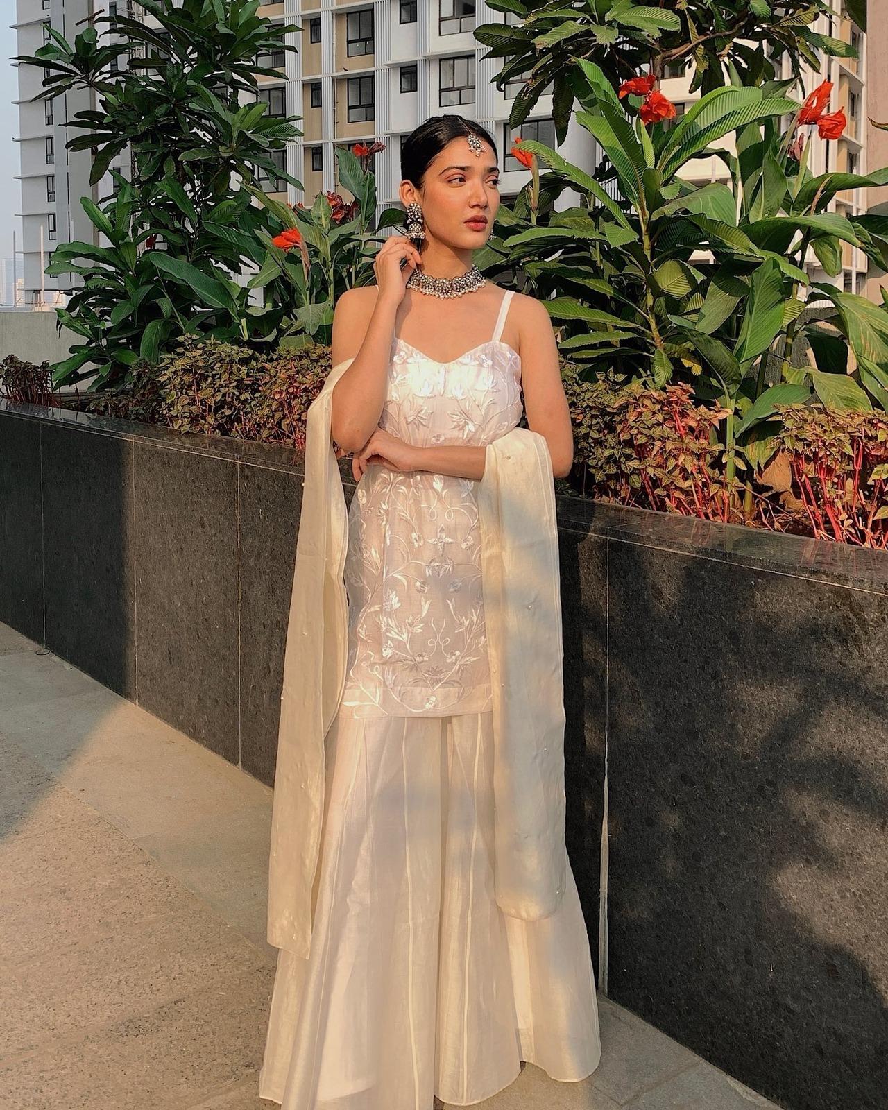 Medha looks divine in this ivory white sharara set featuring a strap-sleeve kurta and a light dupatta. She pairs it with bold silver jewellery and pulls off a fashion statement.