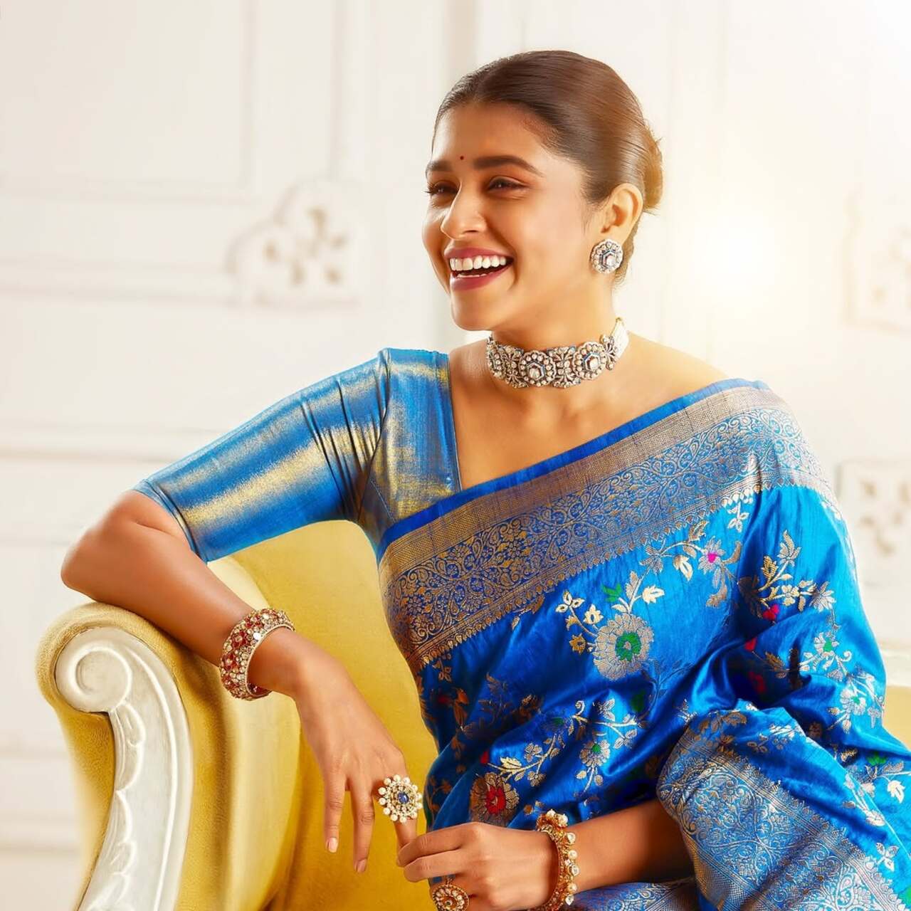 Sanskruti Balgude is wearing a rich royal blue silk saree with golden zari work and floral motifs, paired with a matching blouse with metallic golden sleeves. Her jewellery includes a statement choker necklace, matching earrings, a bracelet, and rings, enhancing her traditional festive look