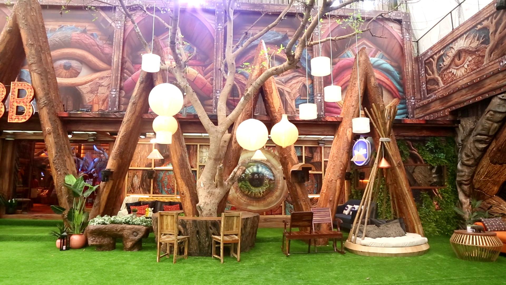 The garden area has a beautiful seating space complete with chairs, tables, and even a small sofa cushion for the housemates, adjacent to the repeating triangular entrance made to look like raw logs of wood.