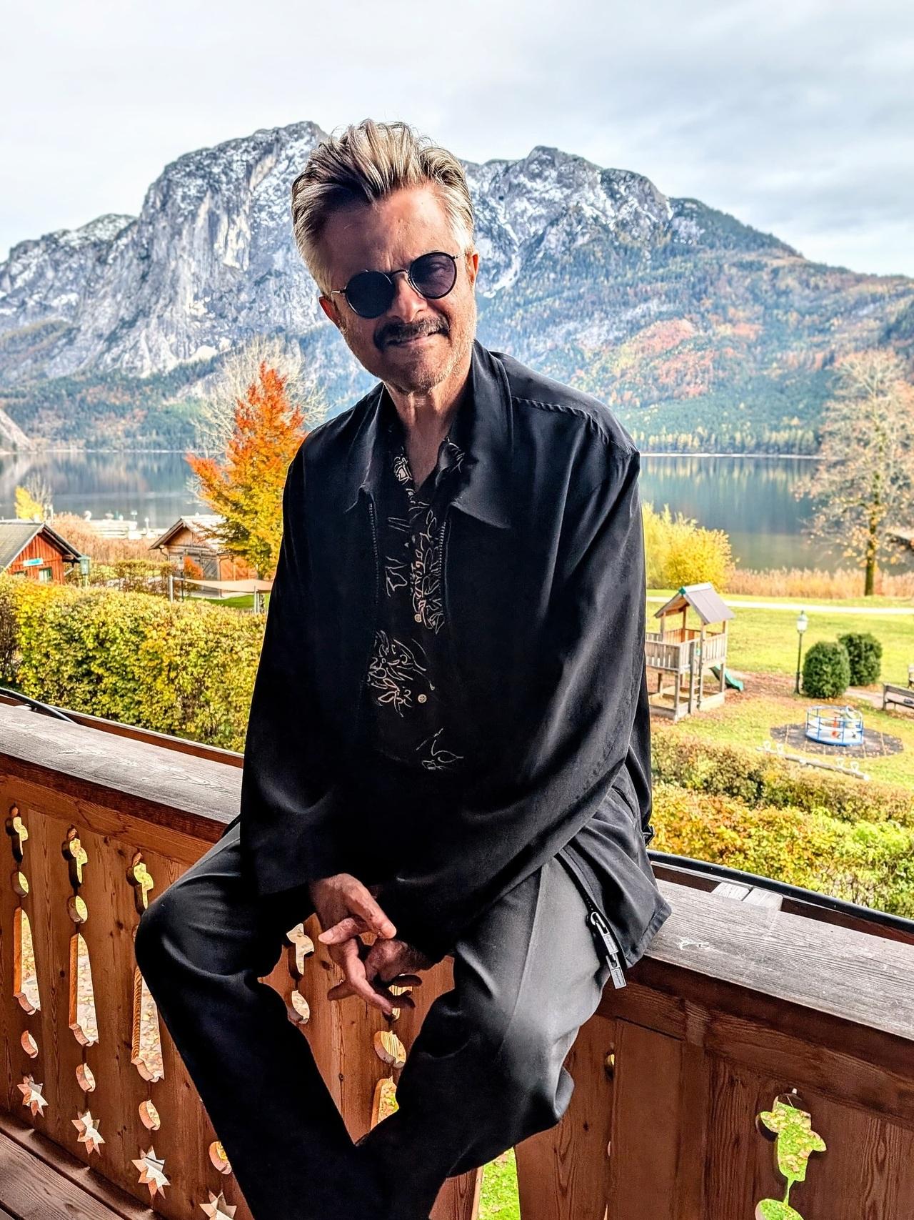 Set against a scenic European backdrop, Anil Kapoor embraces relaxed luxury. The fluid black outerwear, printed shirt, and laid-back posture make this look feel lived-in yet intentional.