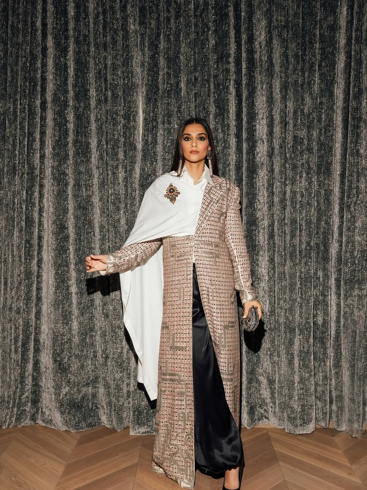 The quintessential fashionista, Sonam Kapoor, stunned in an exceptional ensemble by Anamika Khanna, featuring a long, heavily textured, split coat paired with dark flowy pants and a striking white cape draped over one shoulder. 