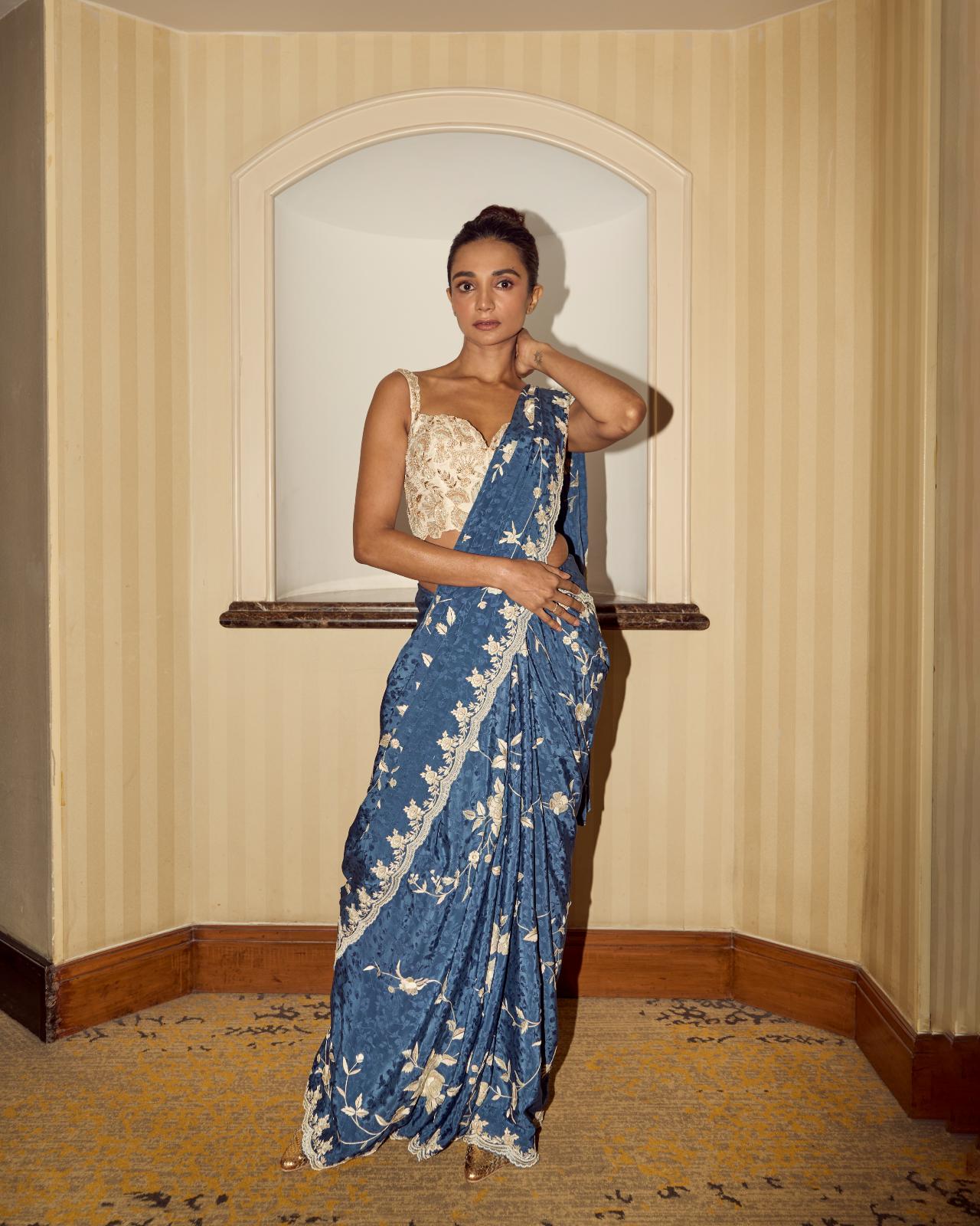 This blue saree adorned with intricate floral embroidery reflects style and sophistication. The embellished ivory blouse adds a unique touch to the outfit.