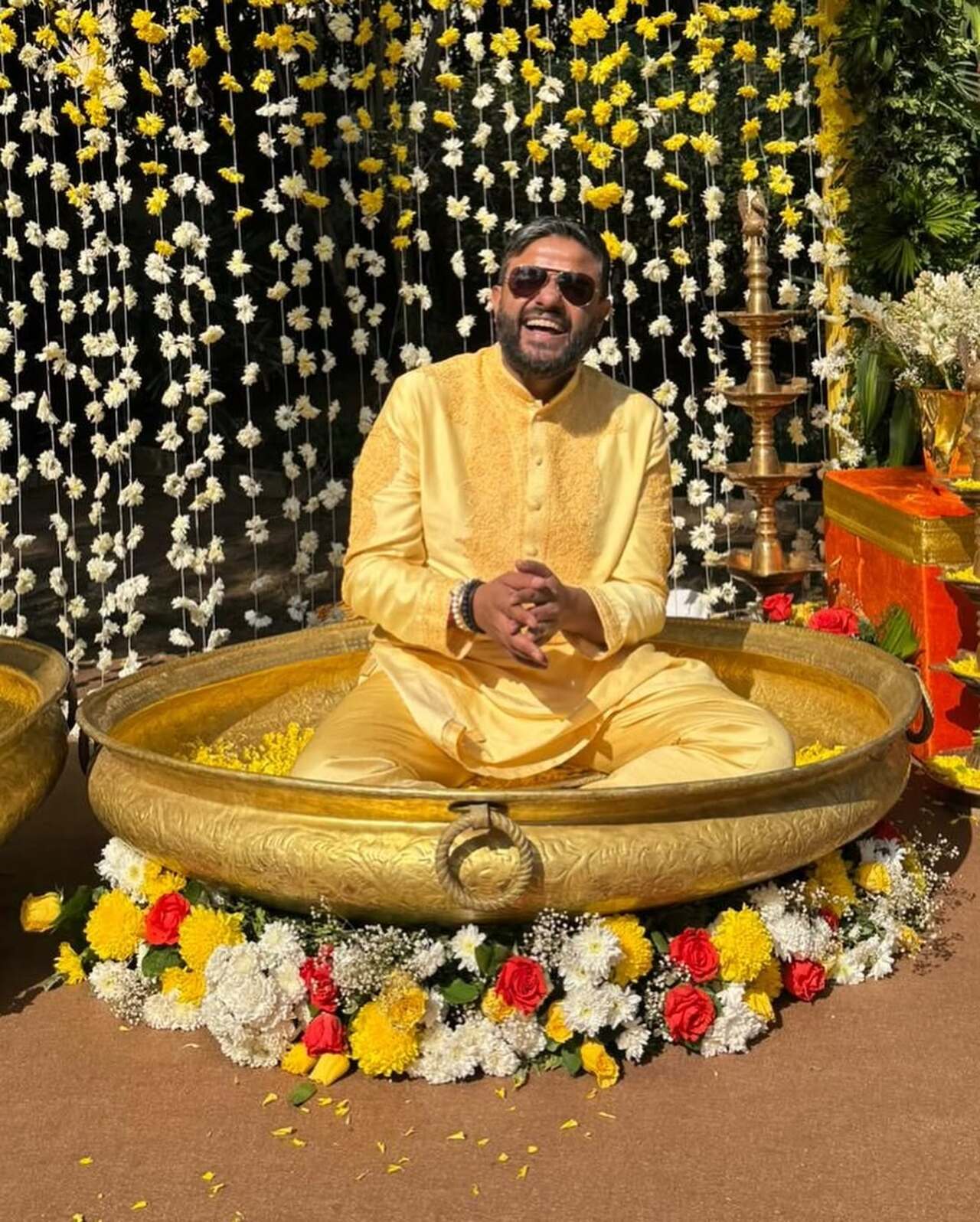 The bride and groom can be seen sitting in tubs as guests apply turmeric on their faces.