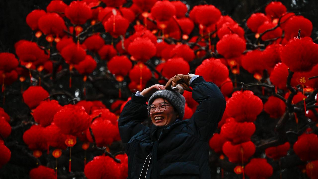 A woman poses for pictures next to red lanterns hanging on trees at Ditan Park in Beijing