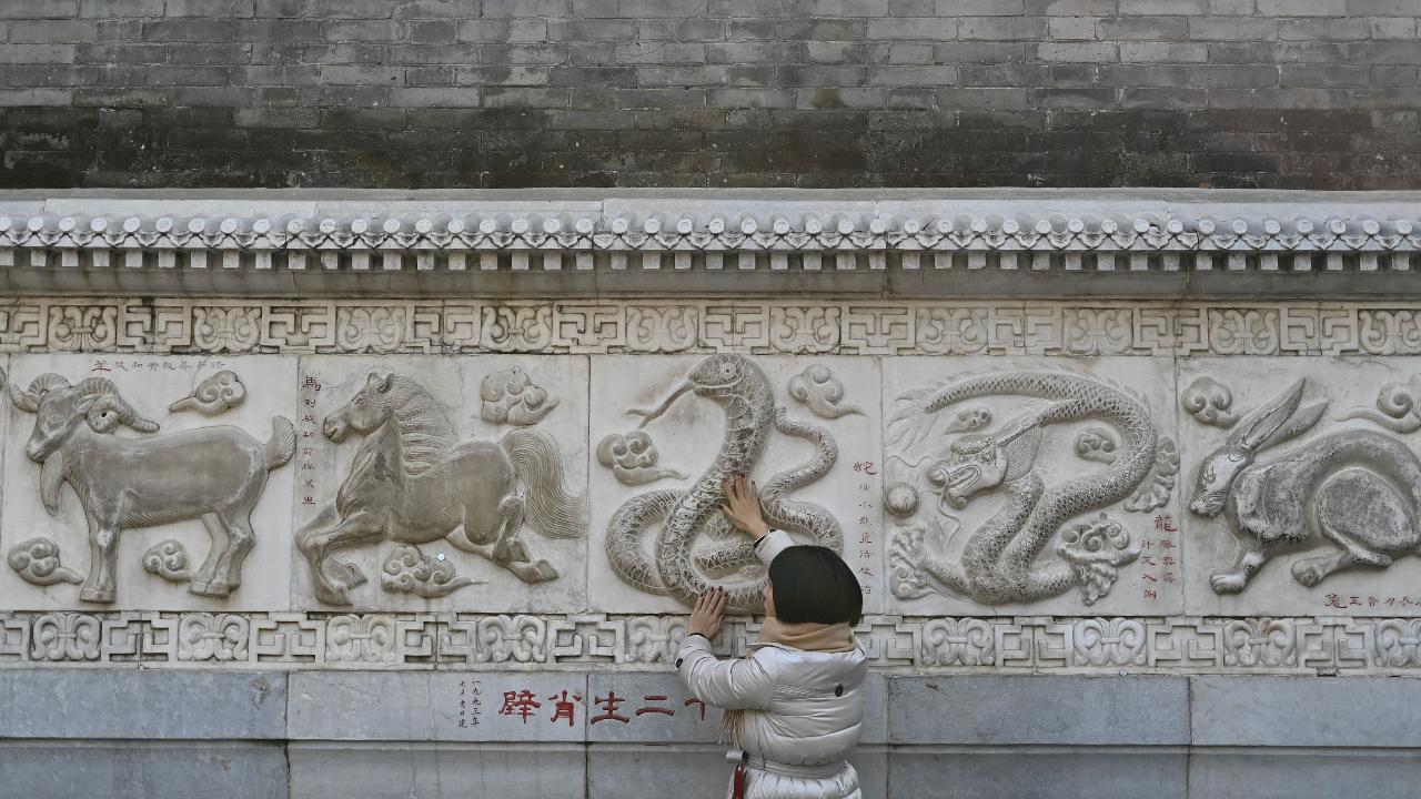 A woman touches the snake figure on the stone wall depicting animals in the Chinese zodiac at the Baiyun Taoist Temple, also known as the White Cloud Temple, in Beijing 