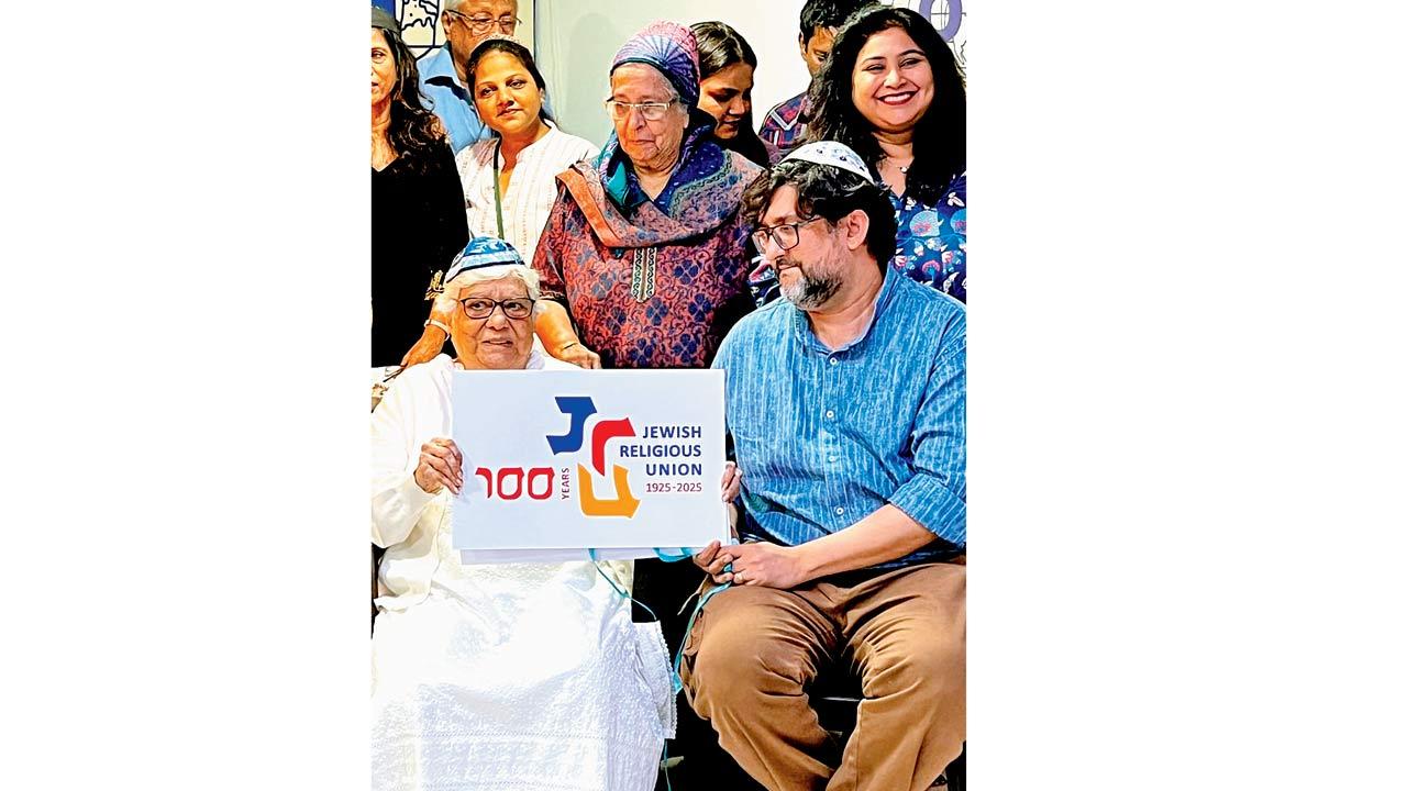 Noreen Elijah unveils the 2025 JRU centenary logo, designed by Brian (seated beside) and Asma Elijah (standing rightmost)