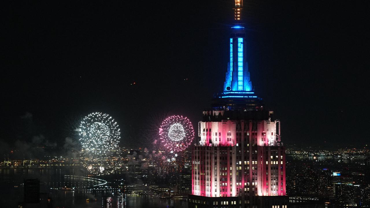 The top of the Empire State Building is lit in Red, White and Blue as fireworks explode above the Manhattan skyline during Fourth of July celebrations in New York City on July 4