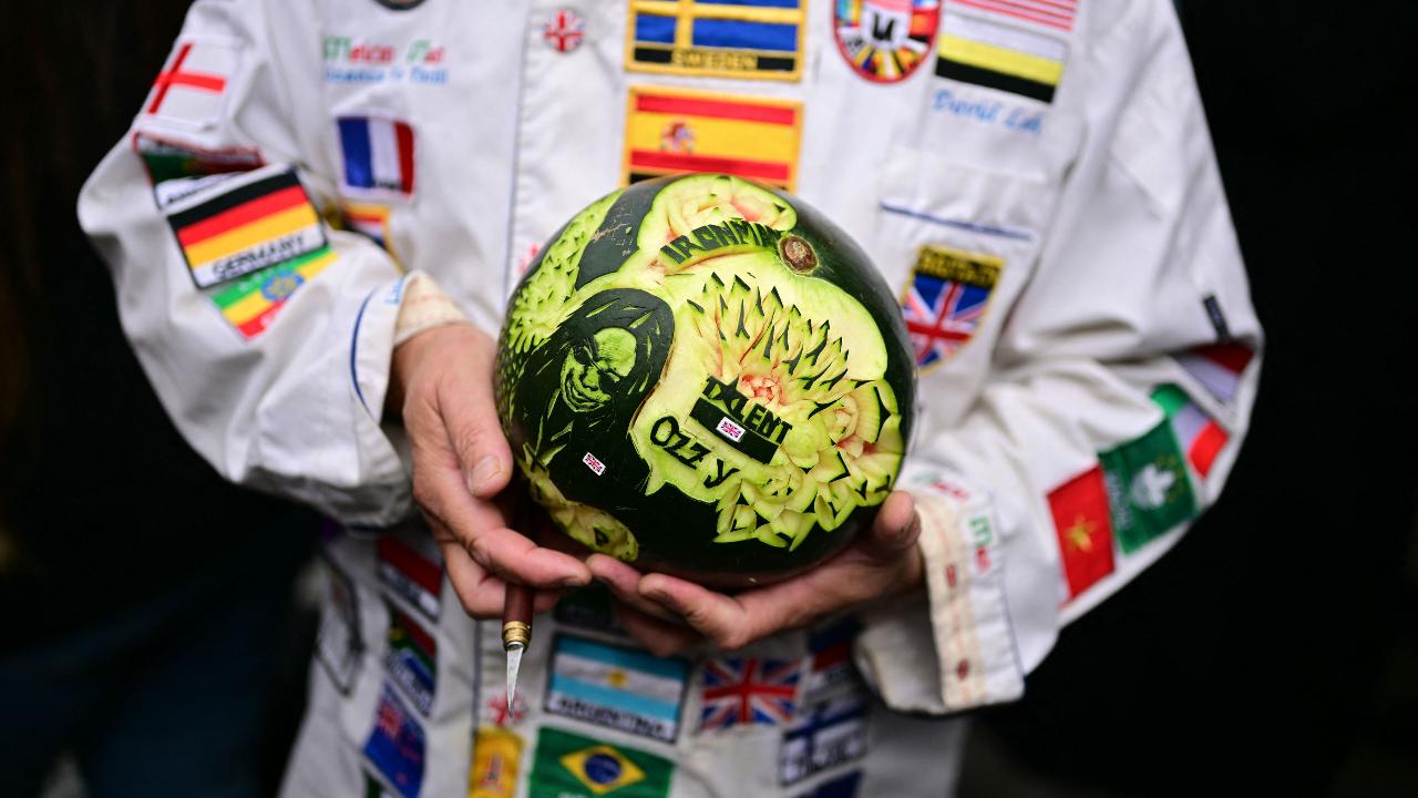 A person holds a melon that they carved an image of the late lead singer of Black Sabbath, Ozzy Osbourne, into as they wait on the streets to pay their respects, before the funeral cortege of the singer makes its way through Birmingham, central England on July 30