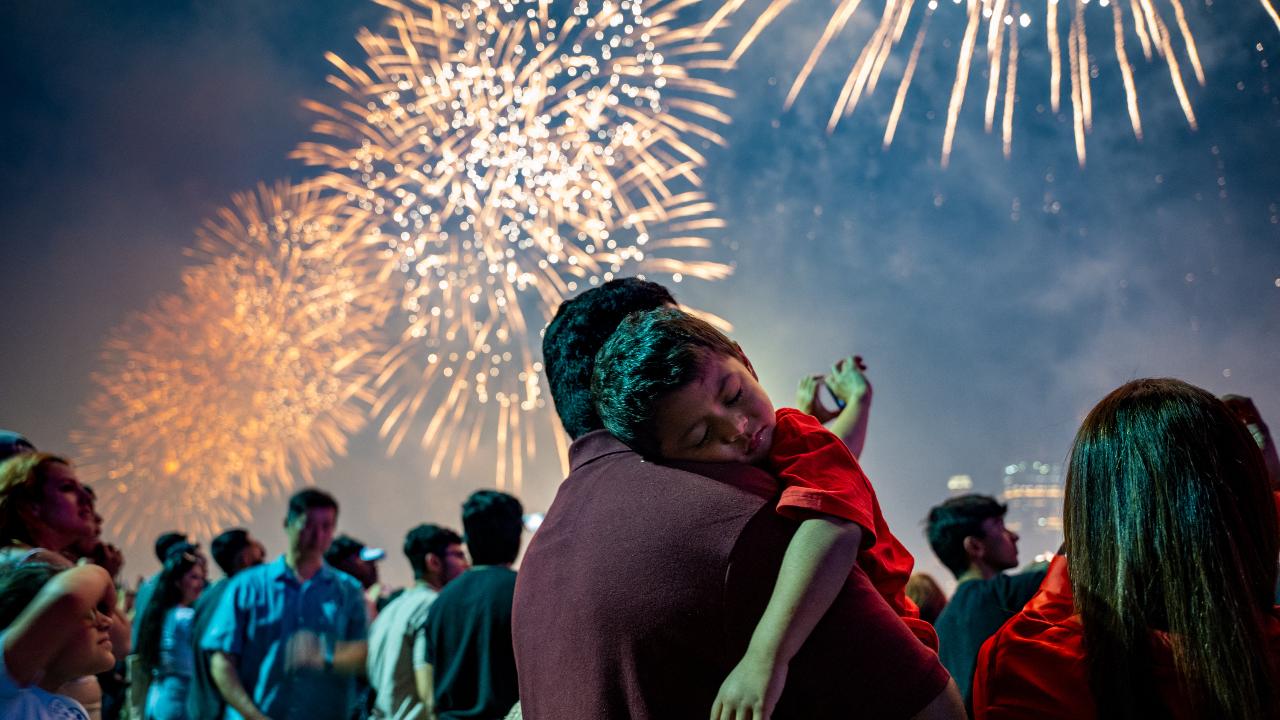 A boy sleeps on his father’s shoulder as fireworks light up the sky during the Macy’s Fourth of July Fireworks celebration on the East River at Brooklyn Bridge Park on July 4 in New York