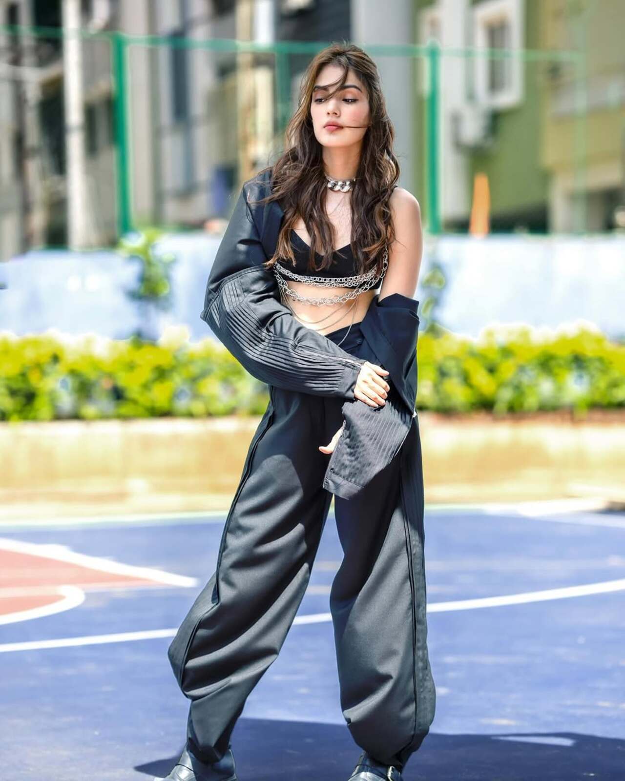 Glossy, grunge, and gorgeously ghetto-fab. Chains drape her like armour over a black bralette and wide-leg co-ord set. With wind-swept hair and heavy boots, this is streetwear’s edgy, editorial evolution