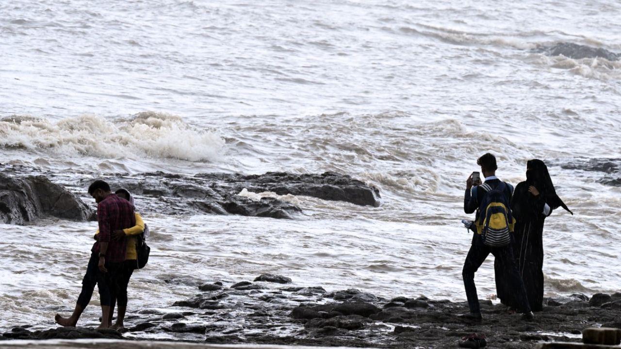 Couples and families soak in the moody monsoon vibes along the rocky coastline, despite rough sea conditions