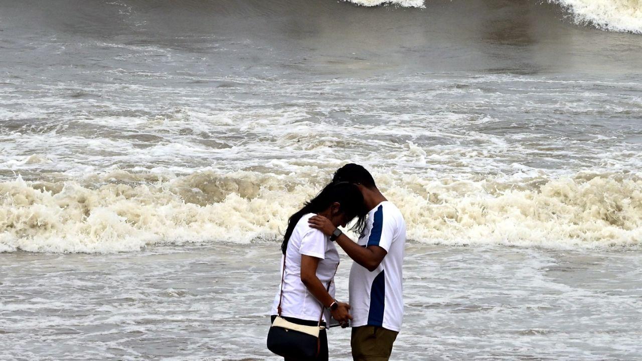 A young couple shares a quiet moment at the beach, standing barefoot on the wet sands as waves crash behind them