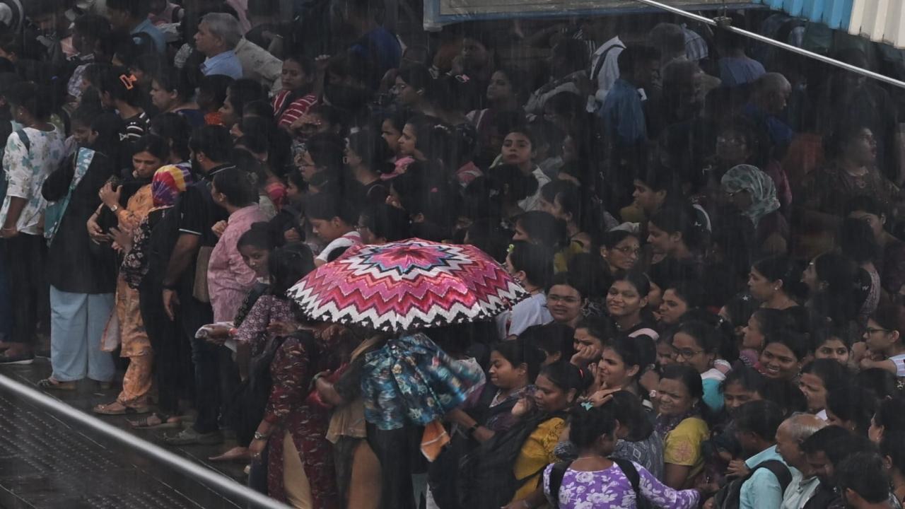 Hundreds of commuters huddle under umbrellas near the station