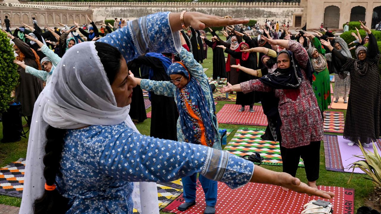 While there are men and women doing yoga, these woman stretch out their mats and get the pose right while covering their head