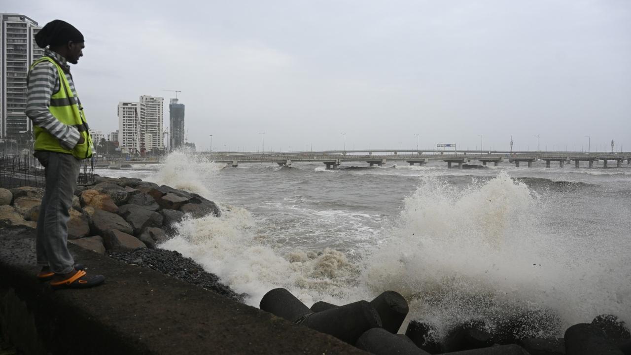 A man stands near the Worli entry point of the Bandra-Worli Sea Link (BWSL) as waves crash against the shore 