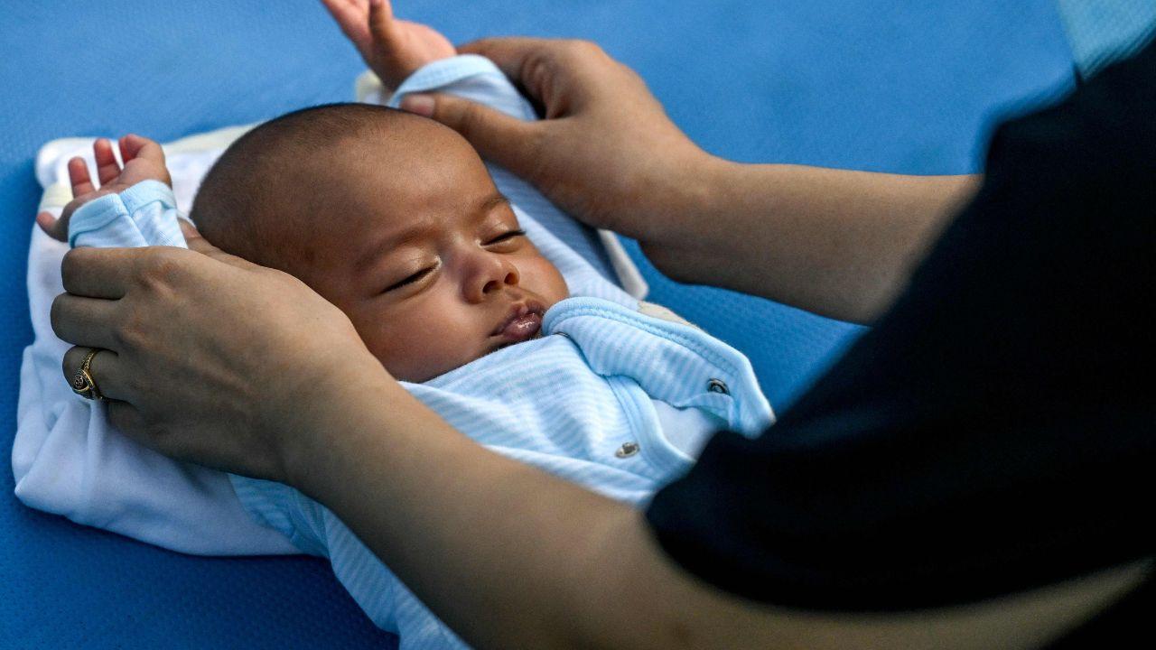 A woman, accompanied by her infant, practices yoga as people gather for a yoga session at Lodhi Gardens in New Delhi