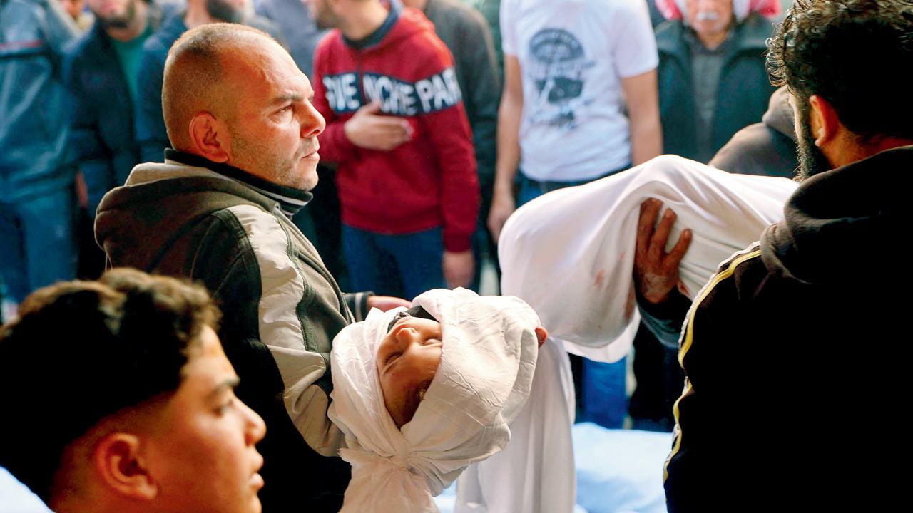 A Palestinian man carries the shrouded body of a child killed in the overnight Israeli airstrike. Pics/AFP