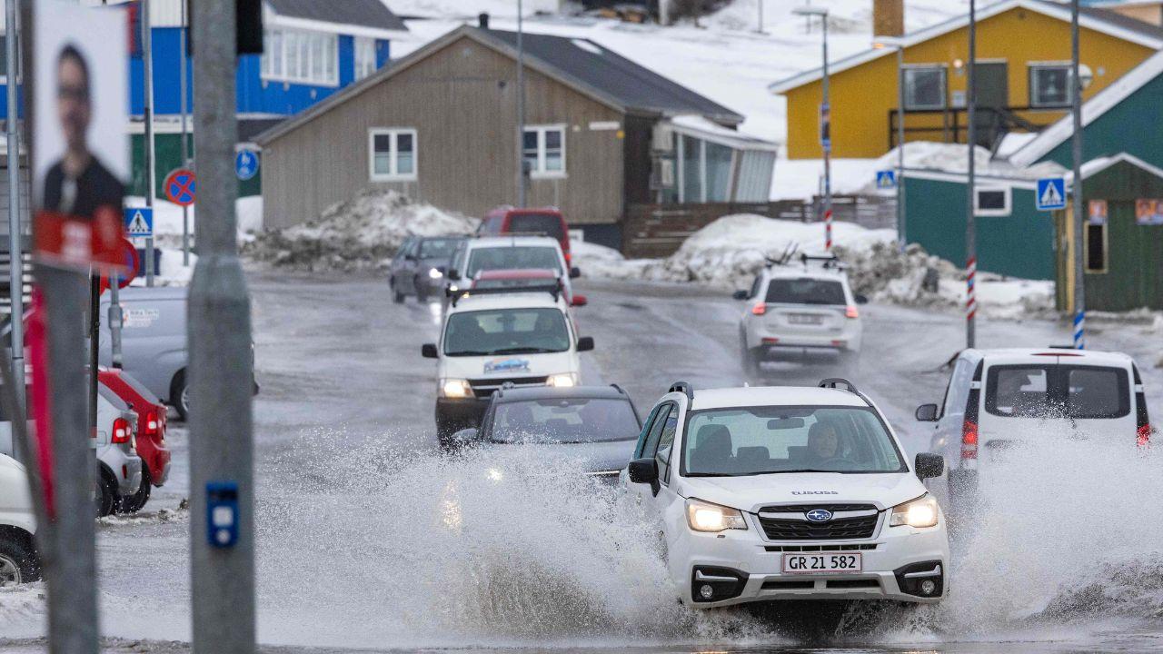 Meltwater is cascaded as cars drive through a puddle in Nuuk
