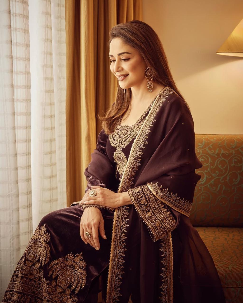 Madhuri Dixit embodies the essence of Eid in a velvet burgundy outfit, featuring golden details along the border and neckline. Keeping it rich yet understated, she exudes royalty and elevates her look with regal jewelry pieces