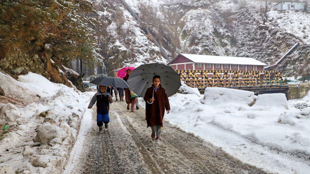 People walk along a snow-covered road in Drung after fresh snowfall in Tangmarg, Baramulla district, North Kashmir