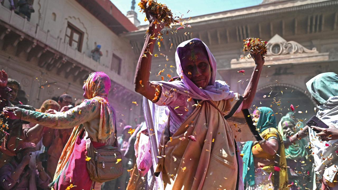 An elderly woman holds a bunch of flower petals in her hand, dances, and enjoys the vibes at the temple