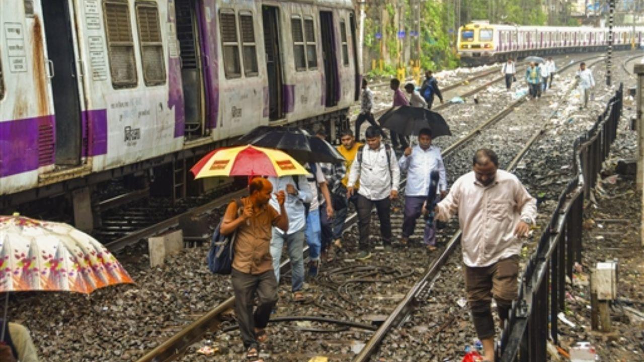 People walk along the railway tracks after several trains were cancelled and delayed in Mumbai