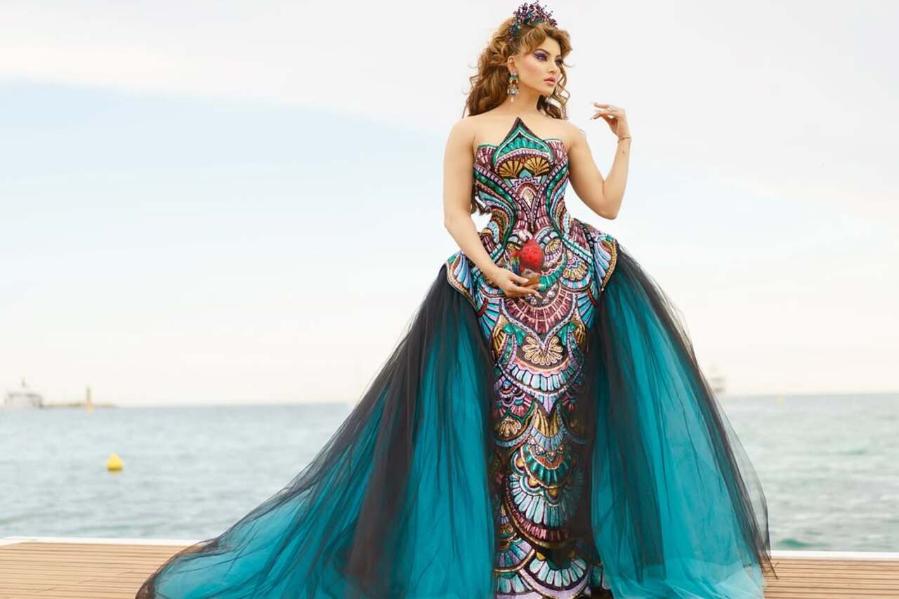 Urvashi Rautela served multiple looks at Cannes. For her first appearance, she opted for a strapless structured outfit in shades of blue, red and yellow to walk the carpet. She completed her look with a matching tiara. She carried a crystal clutch shaped like a parrot which is reportedly worth Rs 4 lakh