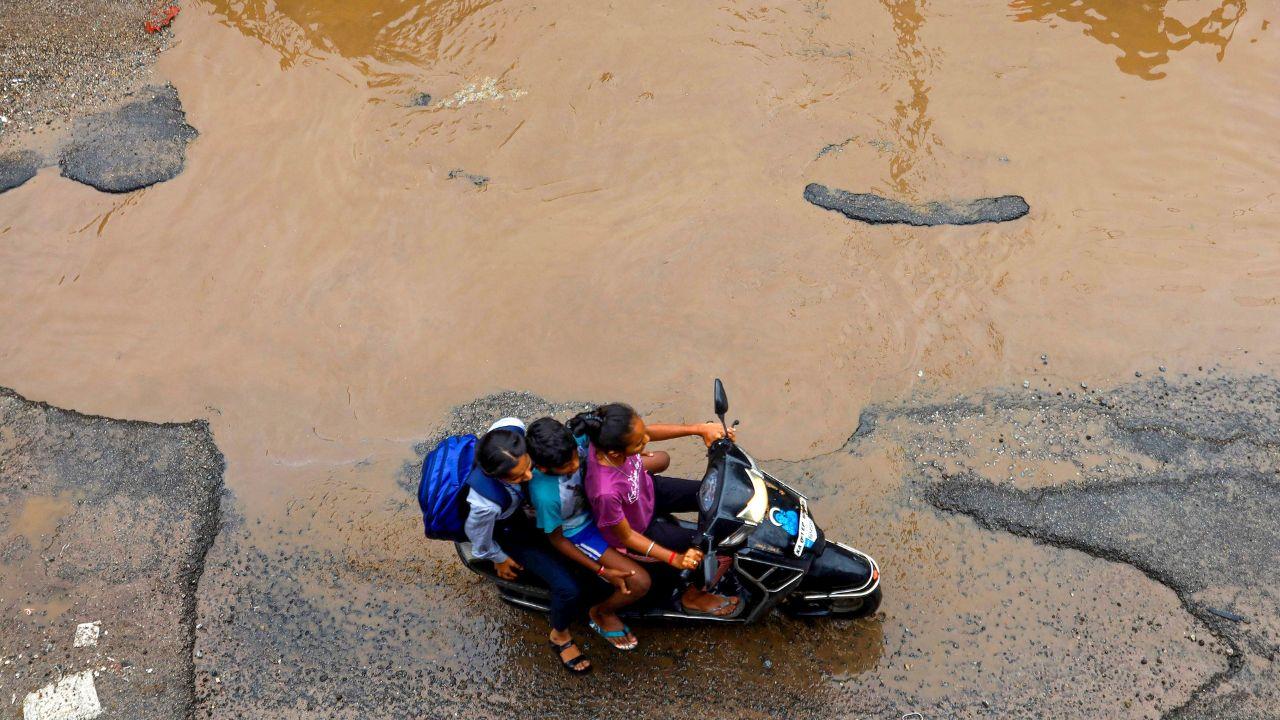 Commuters travel through a damaged road after heavy rains, at Sumanahalli Junction