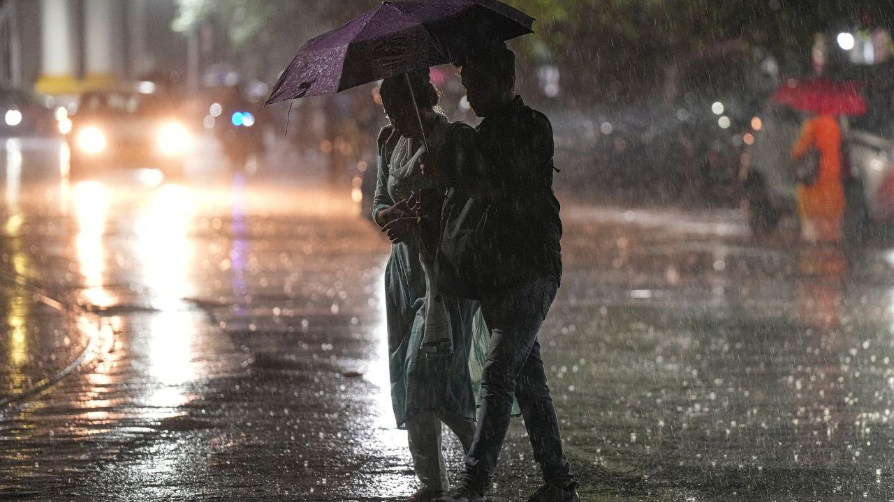 People holding an umbrella cross a road amid rain, in Kolkata, West Bengal