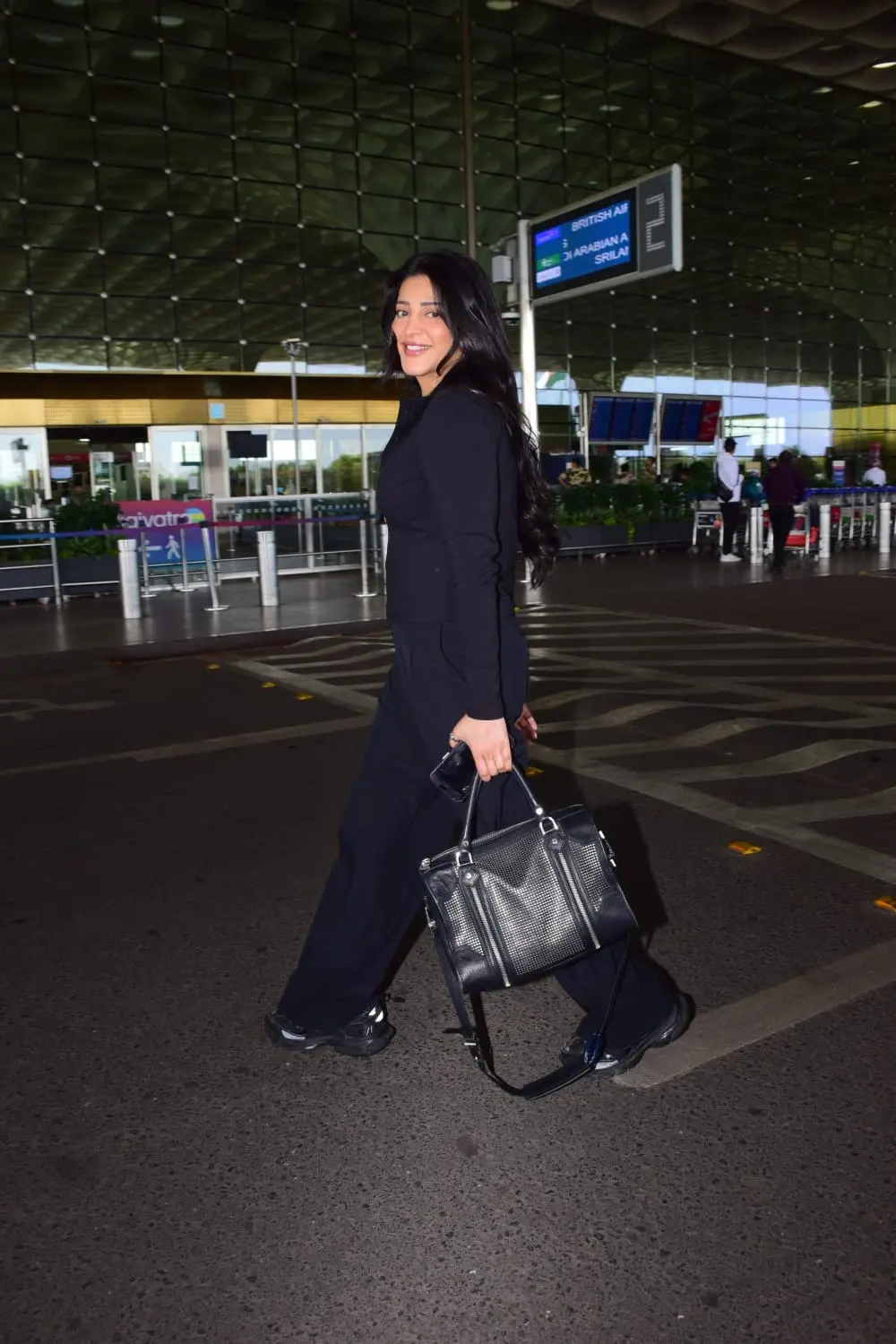 Shruti Haasan was snapped at Mumbai airport this afternoon. She was smiling brightly as she greeted the paparazzi. The actress wore black formals for her airport look