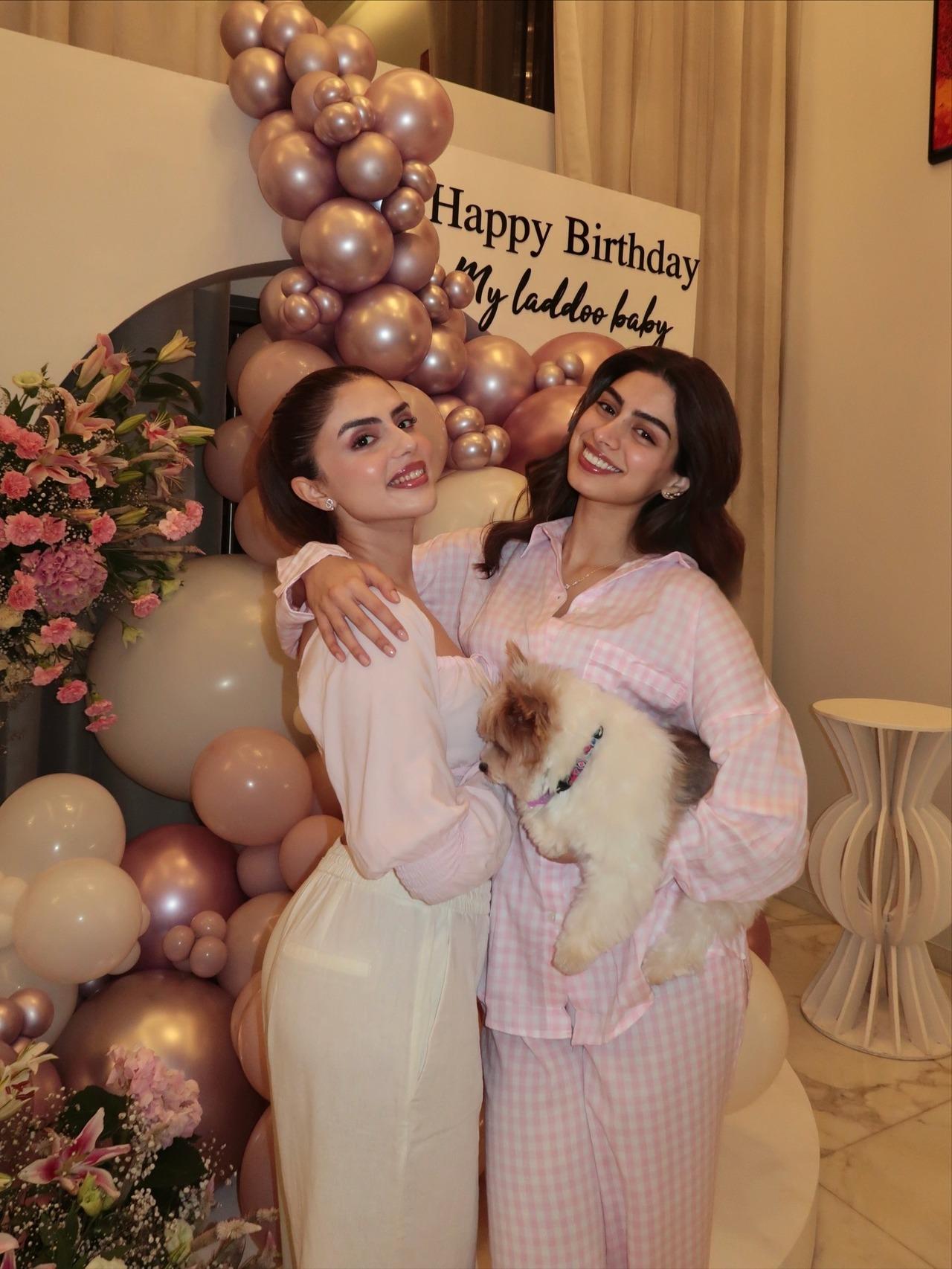 Khsuhi is seen happily posing with her friend and her pet against the balloon backdrop that has the text 'Happy Birthday my laddoo baby' written on it.