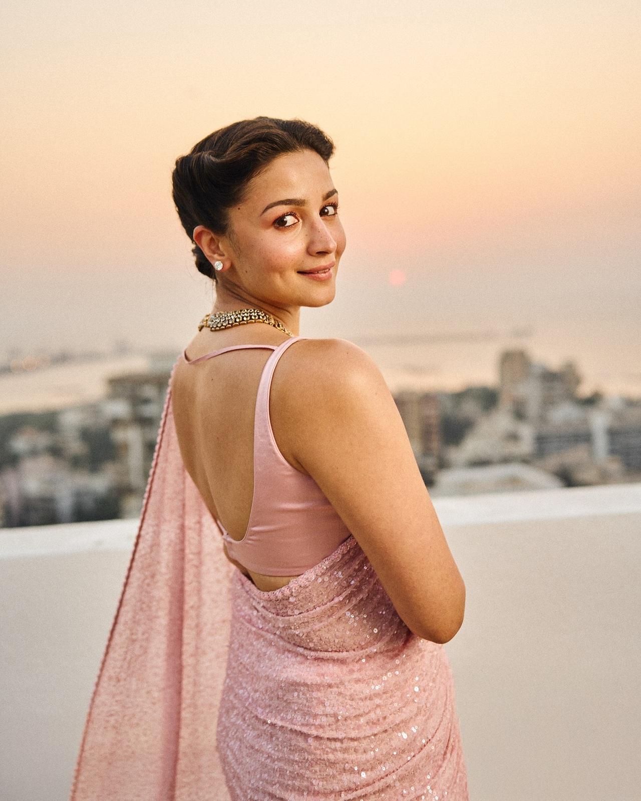 This look of Alia Bhatt is apt for a cocktail party or post-wedding bash. Alia Bhatt dazzled in a pastel pink drape with embellishments and shimmer all across. She paired it with a backless satin blouse, accessorised her look with heavy jewellery and rolled her hair in a smooth bun.