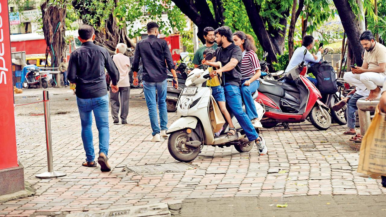 A biker without a helmet rides on the BA Road footpath as several scooters remain parked along it