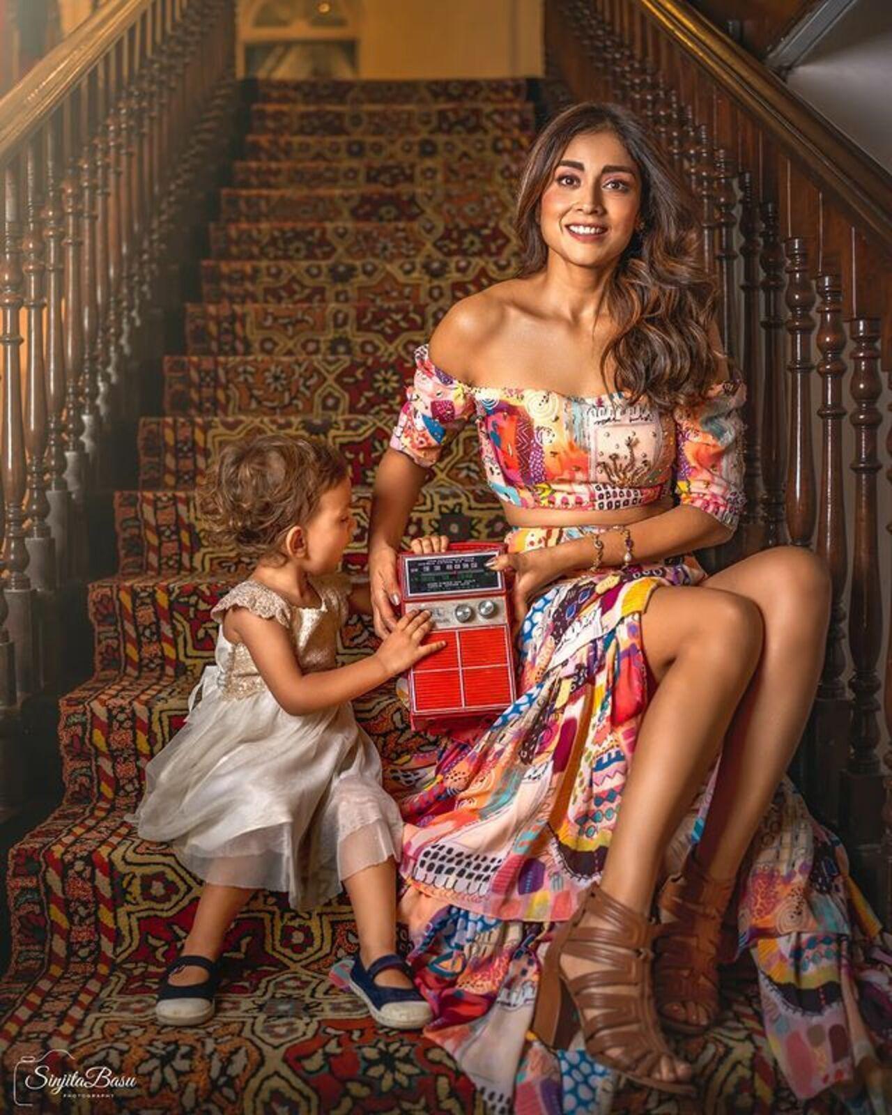 What a gorgeous picture of Shriya with her daughter. Shriya looks glamorous in the colourful sleeveless high-slit dress, as little Radha is busy playing.