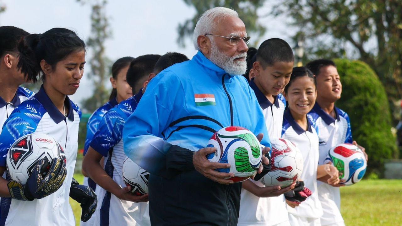 PM Modi shared photos of himself energetically playing football with uniformed young athletes on a scenic grassy field. Pic/X