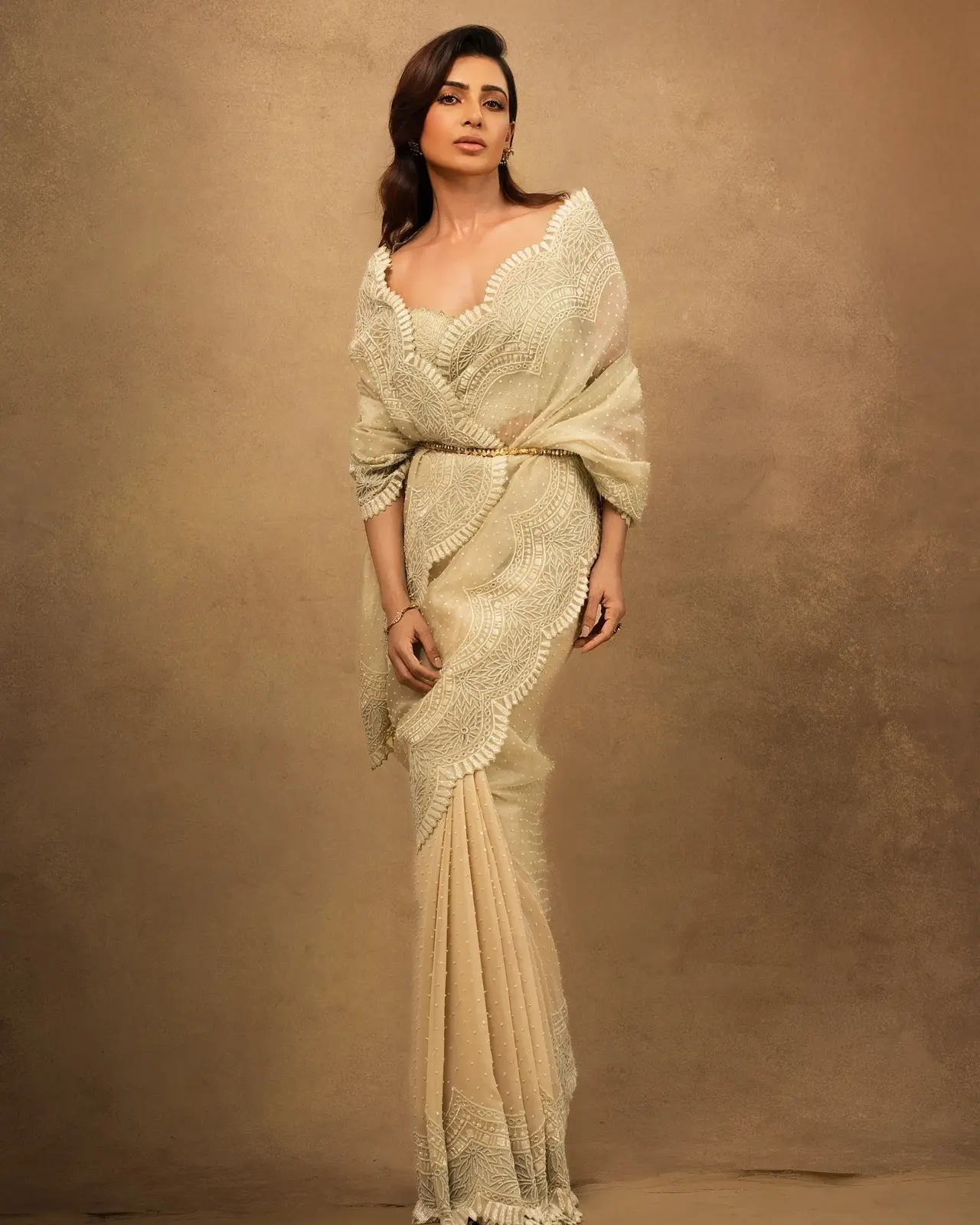 Samantha looks ethereal in this ivory organza saree, which features delicate scalloped borders and intricate embroidery. She adds a modern touch by cinching the waist with a thin gold belt.