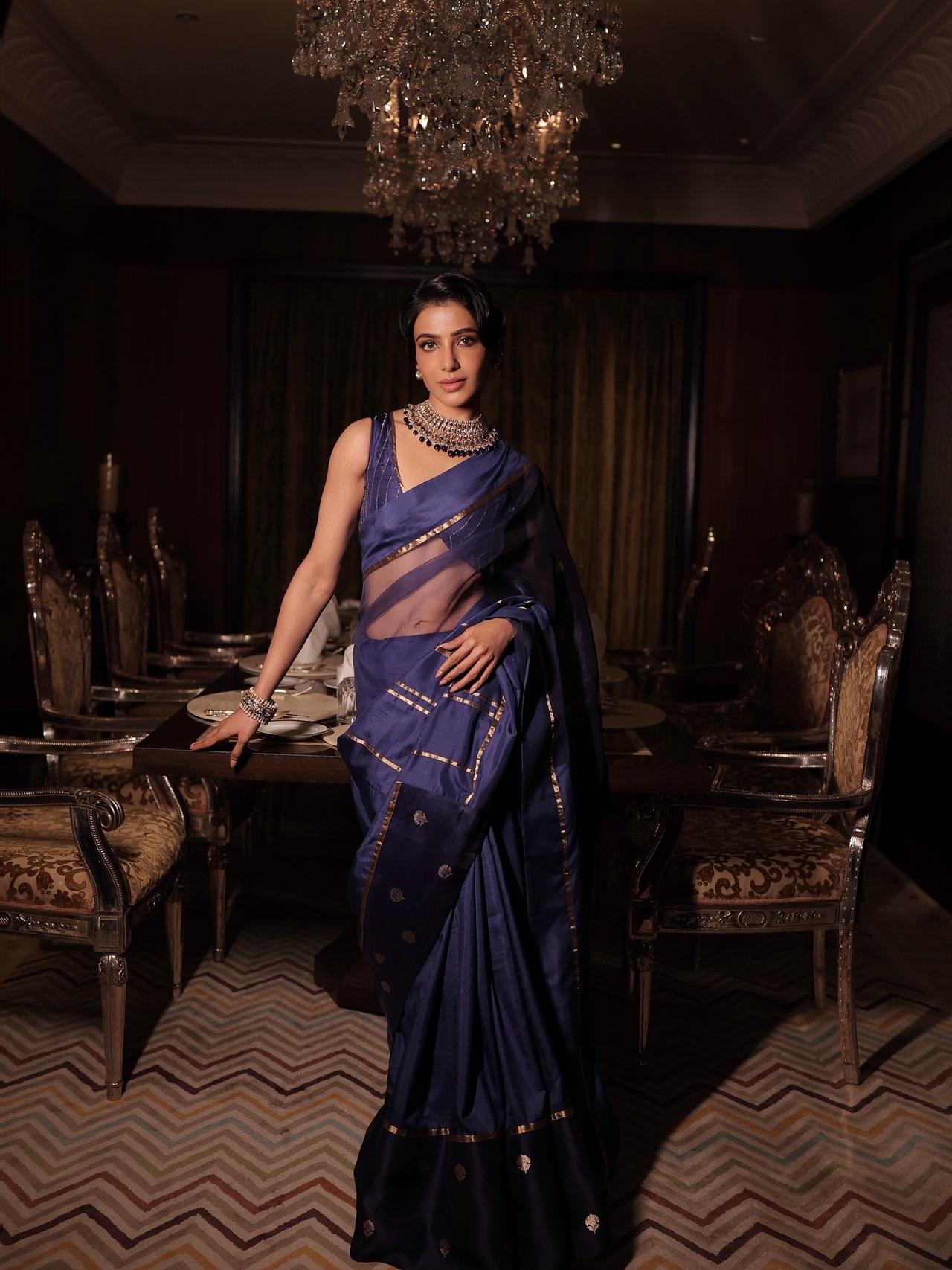 Samantha looks absolutely regal in this deep navy blue saree, which features a beautiful sheer texture and elegant gold accents. She pairs the saree with a matching sleeveless blouse and a stunning statement choker.