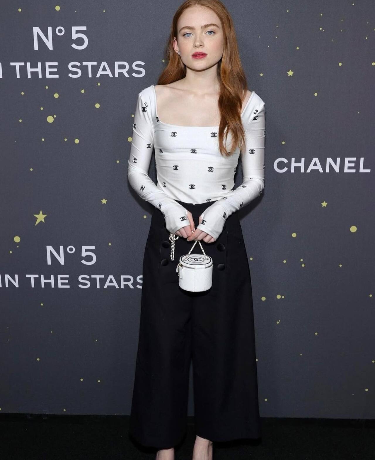 Sadie Sink looks effortlessly chic in this monochrome Chanel ensemble, featuring a white long-sleeved bodysuit, paired with high-waisted, wide-leg black trousers.